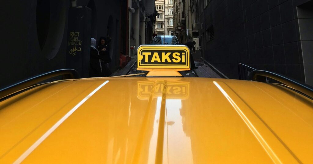 A yellow taxi navigates a narrow urban alley with tall buildings on either side, showcasing city life.